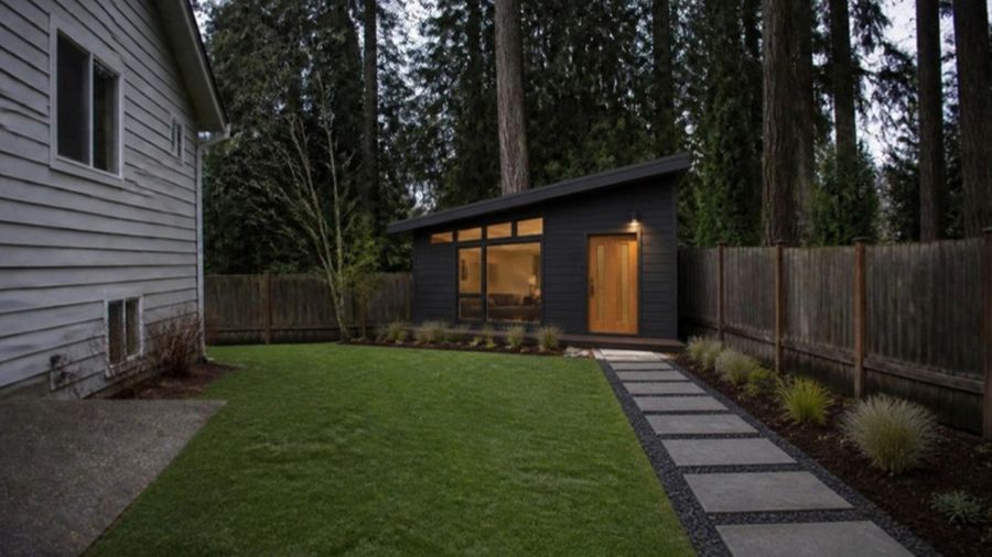 A small backyard home where a shed used to stand, lights on at dusk