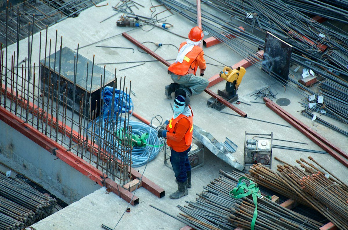 Two workers in orange vests on a concrete deck, tying rebar